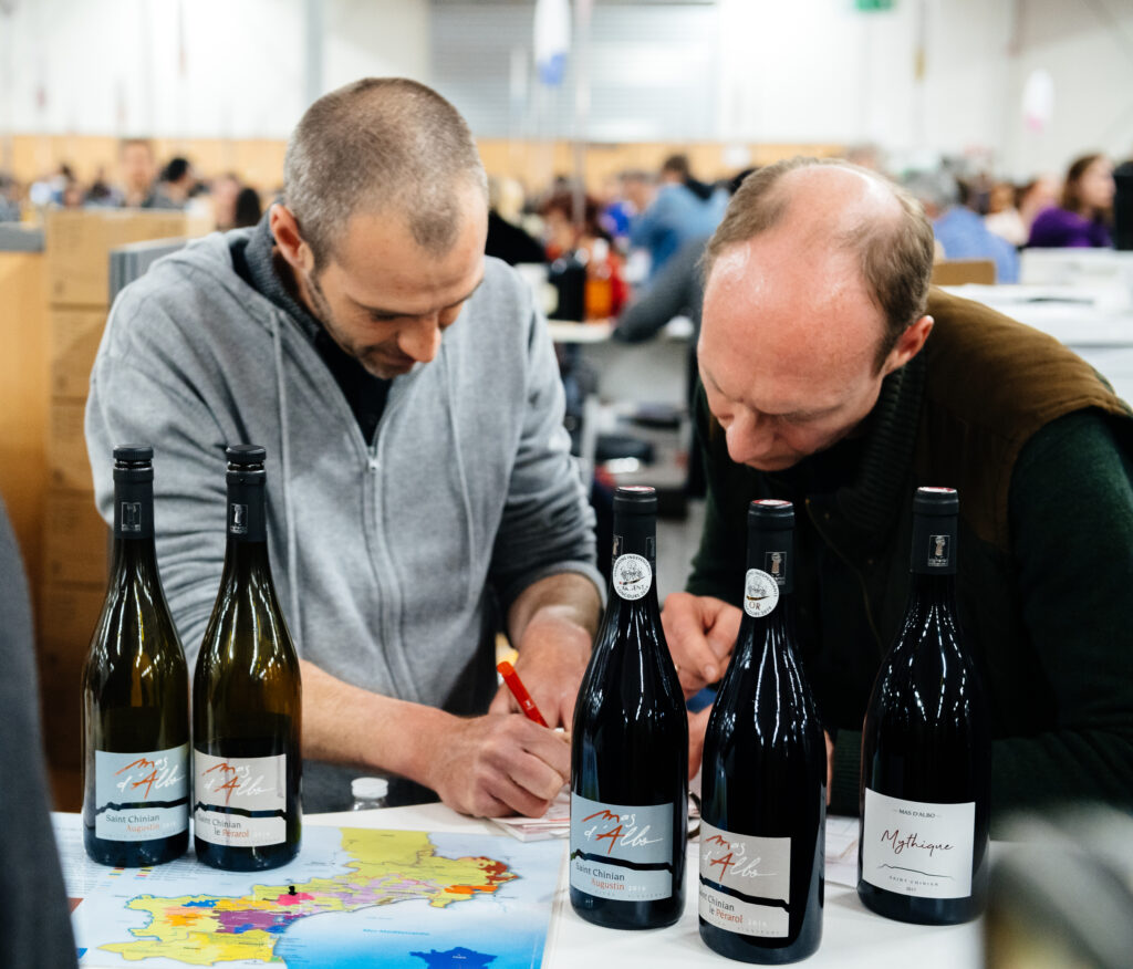 2 men looking at wine bottles on a table with a country map