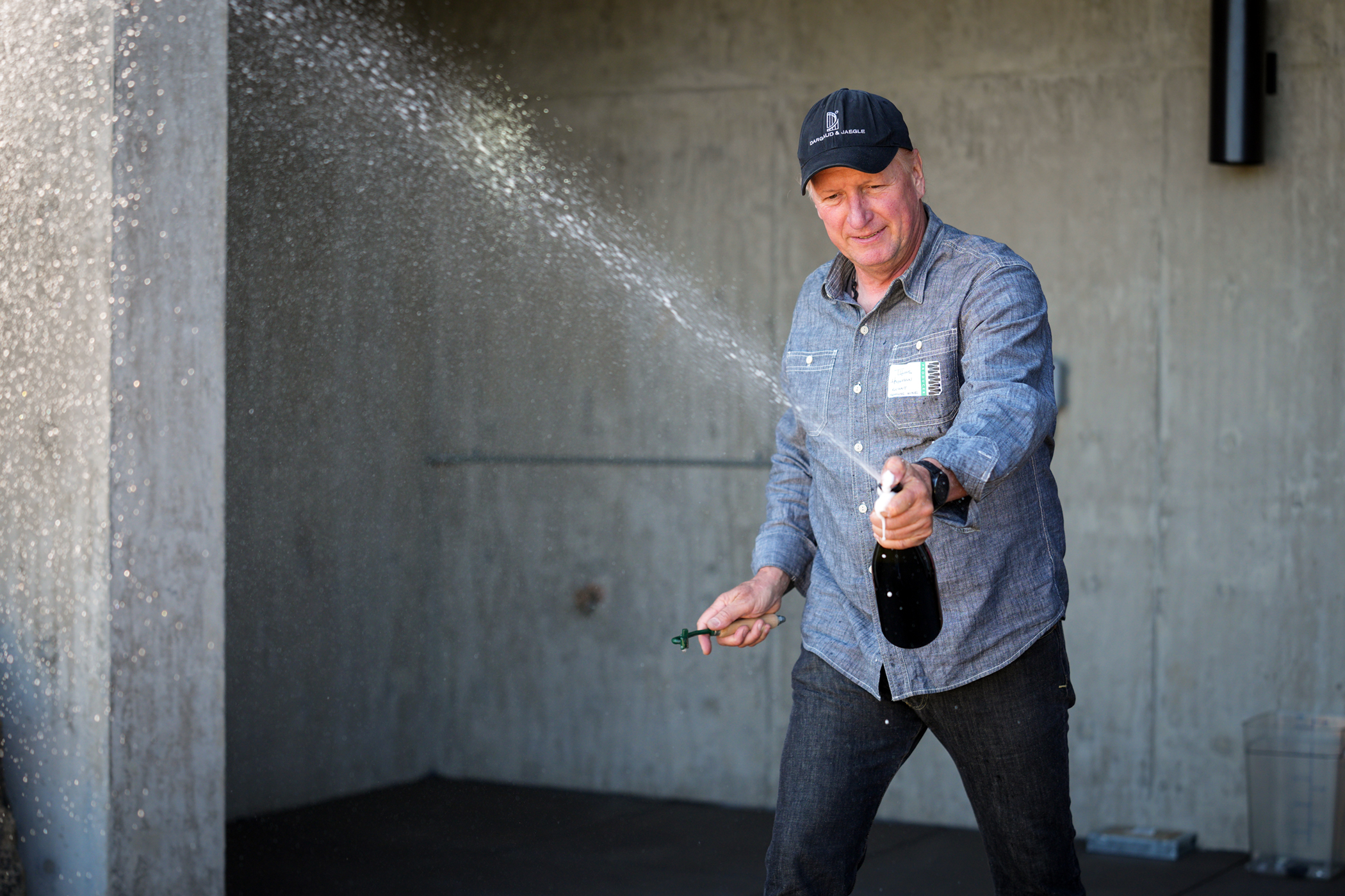 man holding sparkling wine bottle and pushing cork off with his thumb causing the wine to spurt out of the bottle