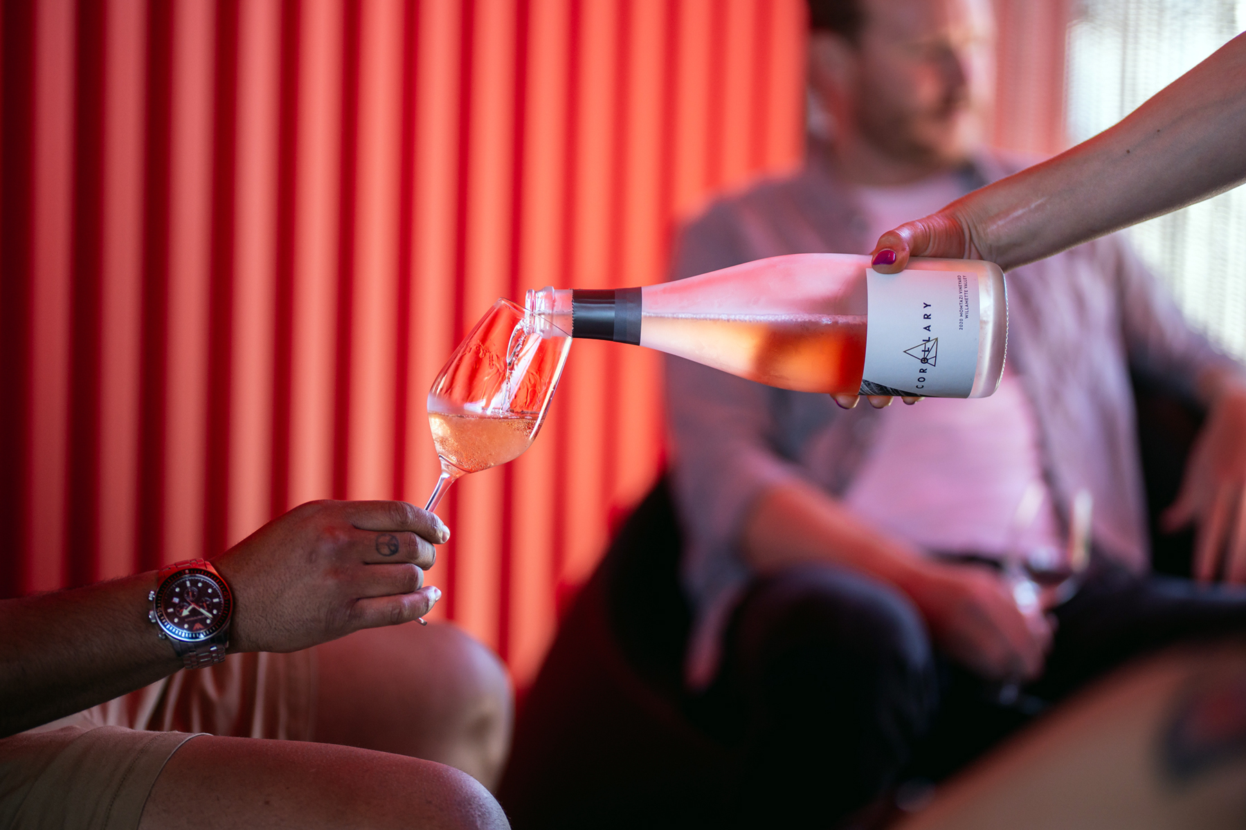person hold wine glass while another person pours from a sparkling wine bottle into the glass
